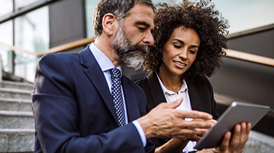 Man in discussion with woman while holding and pointing at mobile tablet device.