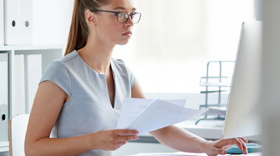 Woman in business attire working at a computer with paper in her hand