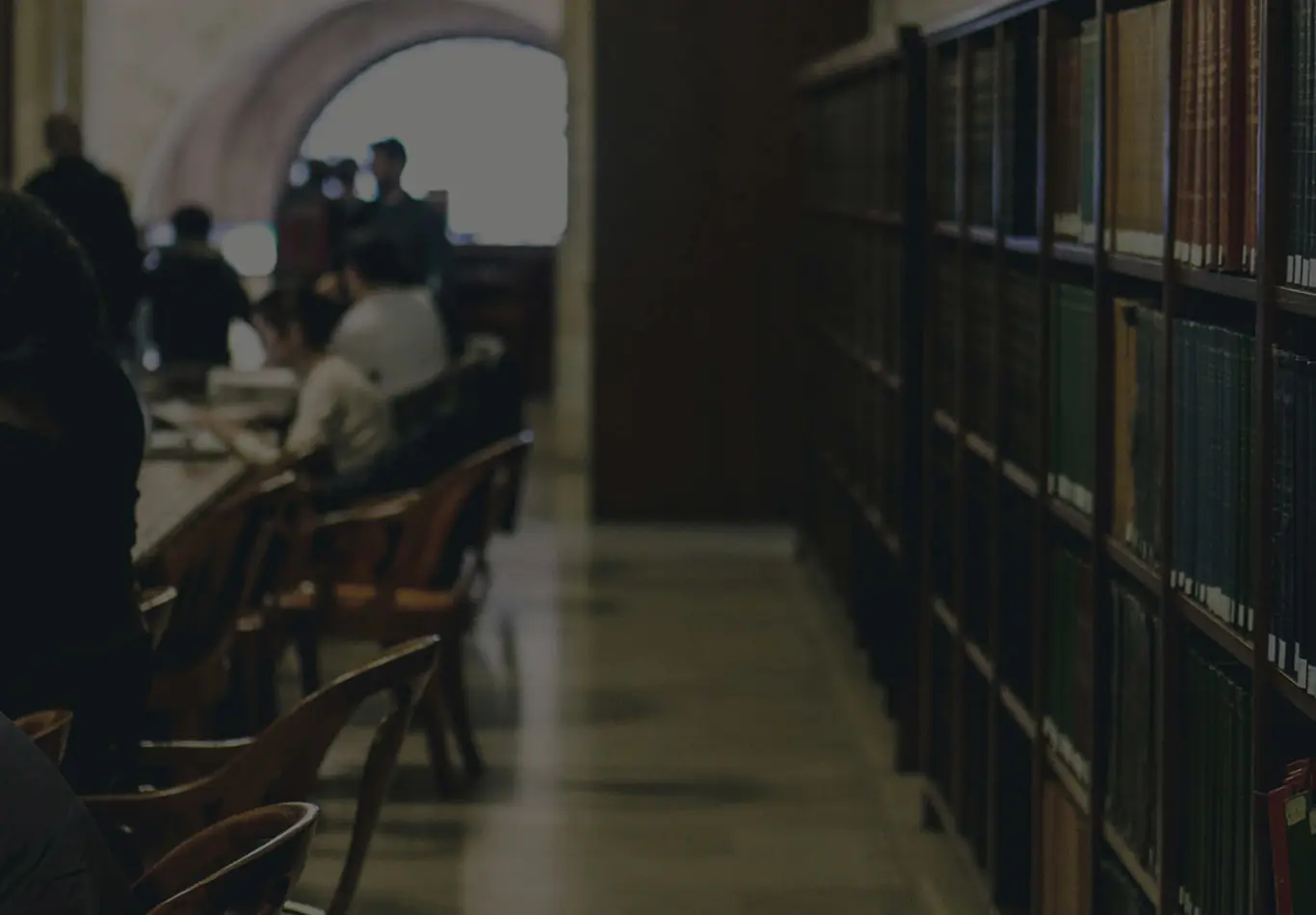 There are a row of books on the right side while people on the left side are sitting down and reading