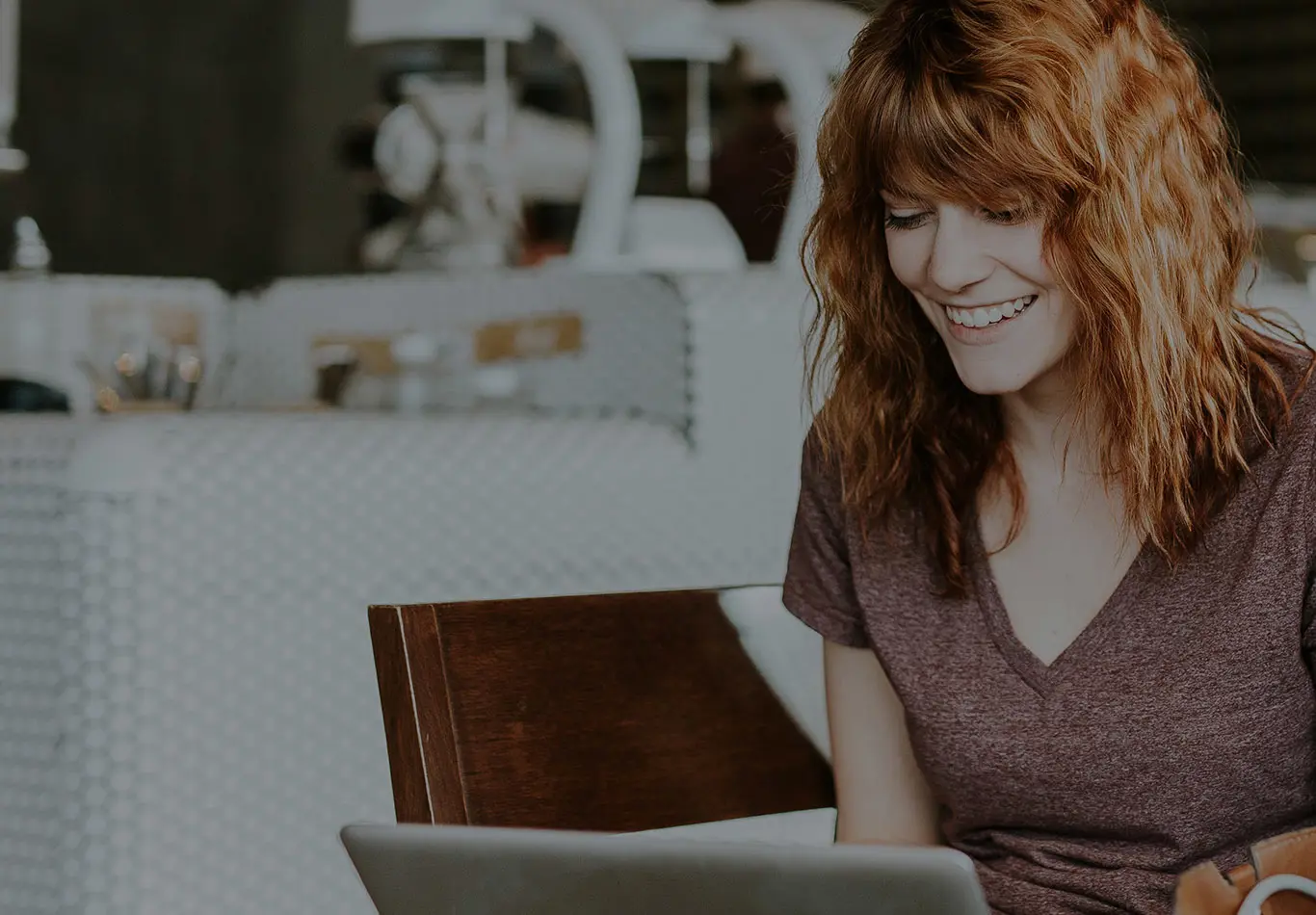 A woman with red hair is looking at her laptop
